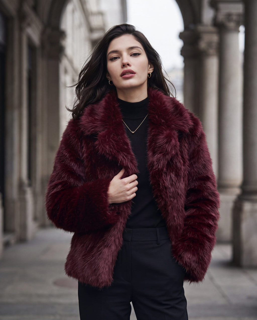 Aveline faux fur jacket in wine red under a stone colonnade in Milan