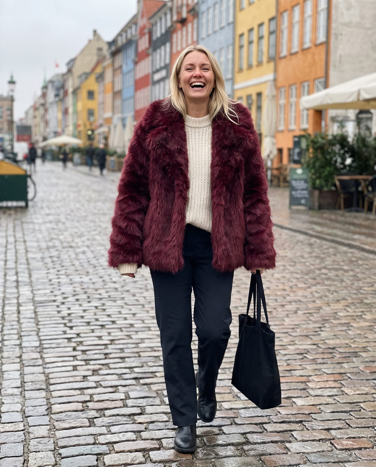 Aveline faux fur jacket in wine red on a cobbled street in Copenhagen